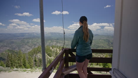 Young-woman-walks-to-end-of-deck-overlooking-mountains-and-forest