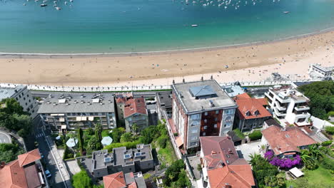 Aerial-drone-shot-flying-over-the-coastal-residential-houses-of-San-Sebastian-tilting-up-to-reveal-the-beautiful-Beach-of-La-Concha-and-the-surrounding-Bay-of-Biscay,-Basque-Country