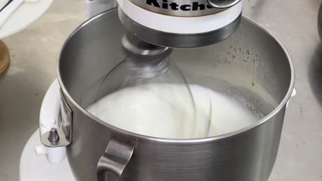 Fluffy-and-soft-Swiss-meringue-buttercream-pastry-making-in-progress,-close-up-shot-of-an-electric-mixer-mixing-and-beating-egg-white-and-sugar-until-it-is-glossy-peak-and-stiff-peak