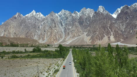 Toma-Cinematográfica-De-Drones-De-Conos-Passu-En-Hunza-Pakistán,-Moviéndose-Hacia-El-Pico-Tupopdan-Con-Un-Tuk-Tuk-Conduciendo-En-La-Autopista-Karakoram,-Toma-Aérea-Amplia