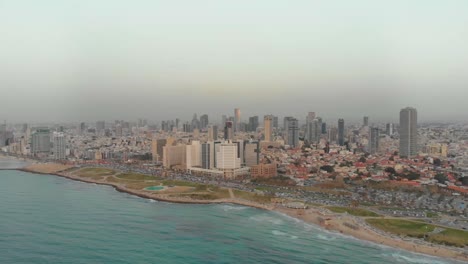 Aerial-view-of-Tel-aviv-beaches-and-charles-clore-park-at-sunset,-Summer-time-with-haze-in-the-air