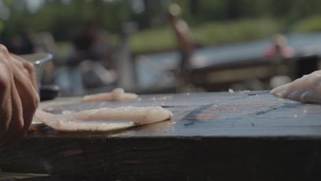 Side-closeup-of-hands-filleting-fish-in-exterior-garden-in-summer,-pan,-day