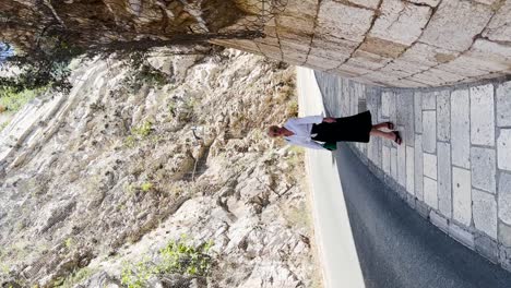 Slow-motion-of-a-young-blonde-girl-dressed-in-a-black-dress-and-white-shirt-walking-along-the-street-beside-the-Old-Town-in-Dubrovnik