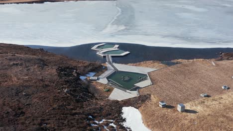 View-of-geothermal-spa-baths-in-Iceland-lake-partially-frozen,-aerial