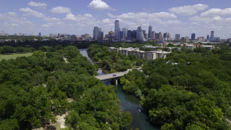 Aerial-view-over-the-Barton-Creek,-with-the-Austin-city-skyline-in-the-background---reverse,-tilt,-drone-shot