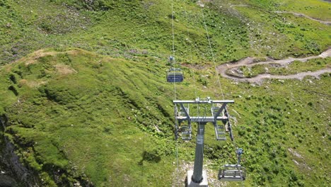 Cable-car-going-up-the-mountain-in-the-swiss-alps,-green-meadows-and-trail-path,-Obwalden,-Engelberg,-drone-aerial-top-view