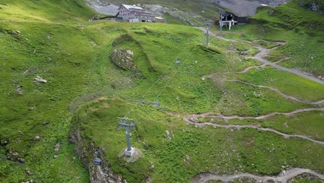 Drone-aerial-view-of-a-large-meadow-and-cable-car-structure-to-go-up-the-mountain,-swiss-alps,-Engelberg,-Obwalden
