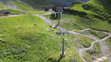 Gondola-installations-in-the-Swiss-Alps,-means-of-transport-to-the-summit-next-to-a-downhill-bike-path,-drone-shot,-tilt-up