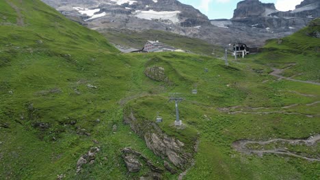 Wide-drone-view-of-a-cable-car-installation-in-the-swiss-alps,-meadows-and-rocky-mountains,-Obwalden,-Engelberg