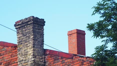 View-of-old-house-rooftop-with-clay-brick-chimney,-roof-covered-with-red-clay-tiles,-sunny-summer-day,-distant-medium-shot