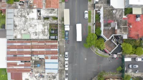 Drone-capture-the-aerial-view-of-the-bus-moving-through-the-neighborhood-of-Guatemala-City-capital-of-Guatemala,-in-Central-America-and-passing-by-many-vehicles