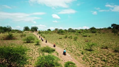 A-Group-Of-Motorcycle-Riders-Driving-On-Dirt-Road-Through-Bushes-In-Kenyan-National-Park,-East-Africa
