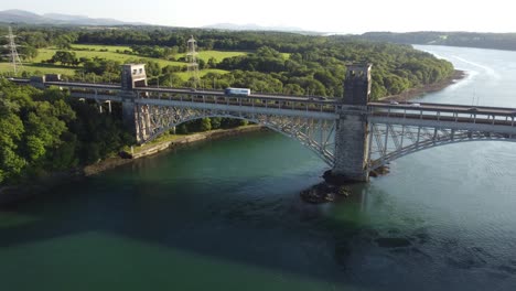 Luftaufnahme-In-Richtung-Pont-Britannia-Bridge-über-Die-Schimmernde-Walisische-Menaistraße-Bei-Sonnenuntergang