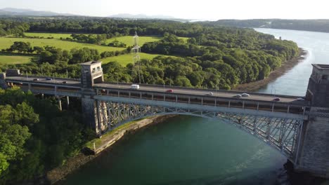 Aerial-view-Pont-Britannia-bridge-over-shimmering-Welsh-Menai-Straits-at-sunset-panning-left-pull-back