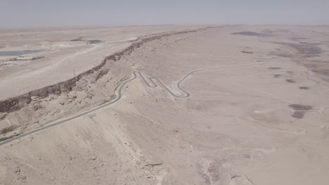Aerial-view-of-a-beautiful-dry-desert-area-with-a-winding-road-rising-out-of-a-crater