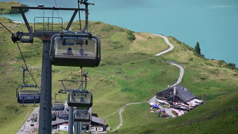 Downhill-gondola-ride-in-the-swiss-alps,-steep-mountains,-flowery-meadows-and-blue-water-lake,-Obwalden,-Engelberg
