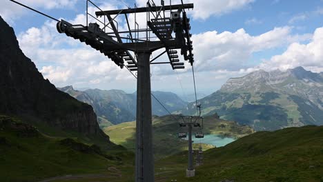Downhill-ride-with-a-chairlift-installation,-majestic-view-on-rocky-mountains-of-the-alps-and-a-blue-water-lake,-Obwalden
