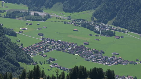Engelberg-village-in-Obwalden,-small-village-near-green-meadows-and-fir-forest,-parachute-over-the-houses,-swiss-alps