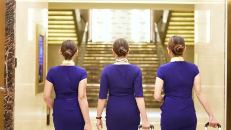 Three-Flight-Stewardesses-Walking-inside-a-Hotel-Wearing-a-Blue-Uniform-Carrying-Luggage-Slow-Mo-4k