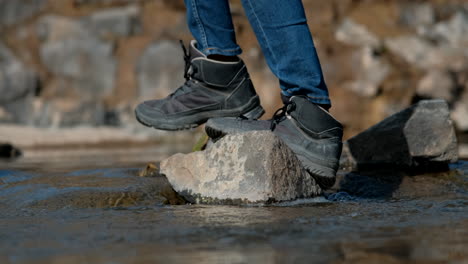 Pies-Con-Zapatillas-Cruzando-El-Río-Pisando-Piedras-Sueltas