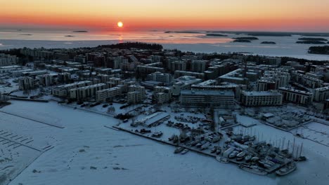 Aerial-view-around-the-snowy-cityscape-of-Drumso,-winter-sunset-in-Helsingfors,-Finland---wide,-panoramic,-drone-shot