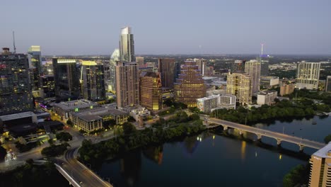 Approaching-lit-uo-skyscrapers-in-downtown-Austin,-dusk-in-TX,-USA---Aerial-view