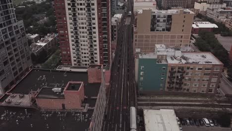 Aerial-footage-of-moving-L-train-in-Chicago,-Illinois-panning-up-towards-skyline