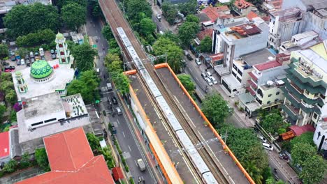 Antena-De-Arriba-Hacia-Abajo-Del-Metro-De-Tren-Elevado-Que-Llega-A-La-Estación-En-Yakarta,-Indonesia