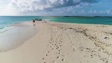 Freunde-Genießen-Sonnenuntergang-Betrachten-Wellen-Auf-Paradiesinsel-Mit-Weißem-Sandstrand,-Drohnenaufnahme