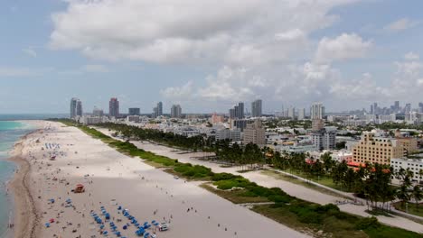 Tropical-sandy-beach-and-Miami-skyline,-aerial-drone-fly-forward