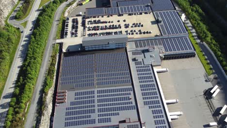 Massive-Solarpanel-Installation-Auf-Asko-Industriegebäude-In-Arna,-Norwegen---Aufwärtsbewegung-Der-Antenne-Mit-Autobahn,-Die-Auf-Der-Linken-Seite-Vorbeiführt