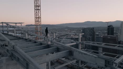 A-young-adult-male-stands-on-a-skyscraper-in-Downtown-Los-Angeles-at-Sunrise-1