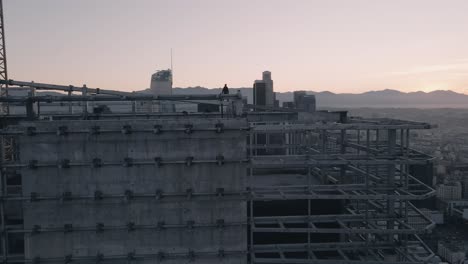 A-young-adult-male-stands-on-a-skyscraper-in-Downtown-Los-Angeles-at-sunrise