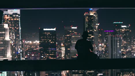 Young-adult-sitting-on-ledge-of-skyscraper-uses-his-phone-to-record-downtown-Los-Angeles