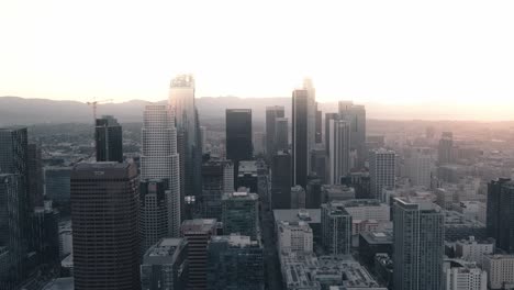 A-young-adult-male-stands-on-a-skyscraper-in-Downtown-Los-Angeles-at-sunrise-raising-his-hands-as-a-drone-zooms-past