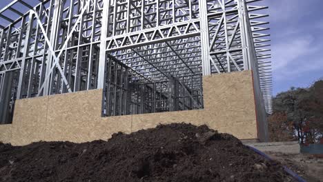 Tilt-up-shot-of-pile-of-soil-in-front-of-steel-frame-house-at-construction-site