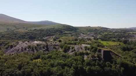 Dorothea-disused-overgrown-slate-mining-quarry-in-lush-dense-Snowdonia-mountain-woodland-aerial-view-panning-left