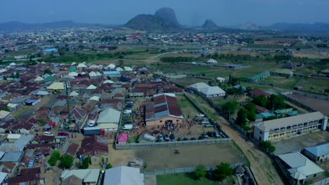 Deidei-area-of-Abuja,-Nigeria-at-dusk-as-people-come-out-of-a-makeshift-church-building---aerial-descending-view