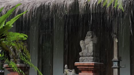 Monsoon-raindrops-at-traditional-tropical-bali-house,-laughing-buddha-statue