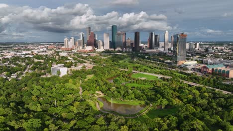 Aerial-view-over-a-park-towards-the-city-center-of-Houston-city,-golden-hour-in-USA