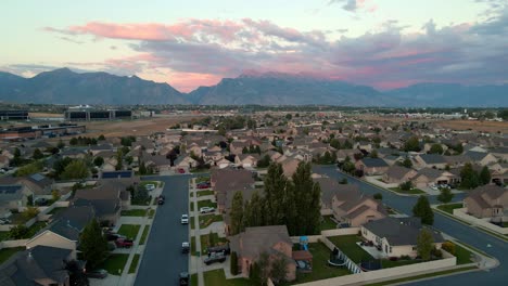 Sliding-aerial-view-of-a-suburban-neighborhood-at-sunset-in-a-valley-beneath-the-Wasatch-Front-Mountains-in-Lehi,-Utah