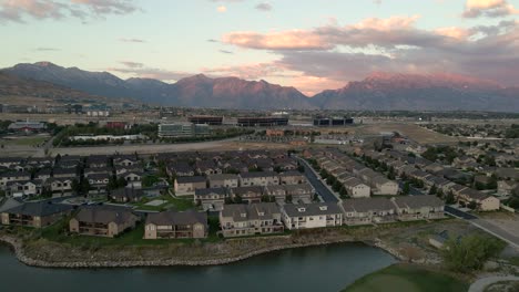 Suburban-neighborhood-by-a-pond-at-sunset-with-business-offices-under-the-mountains-of-the-Wasatch-Front---aerial-flyover