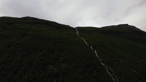 Aerial-view-around-a-waterfall-in-a-mountain-valley,-rainy-day-in-Norway---circling,-tilt,-drone-shot