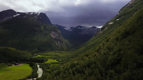 Vista-Aérea-Cerca-Del-Bosque-De-Montaña,-En-Un-Valle-Soleado-Con-Nubes-Dramáticas,-En-Noruega---Al-Revés