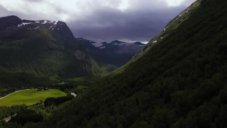 Aerial-view-flying-over-hillside-trees,-towards-a-rainy-valley,-in-partly-sunny-Norway