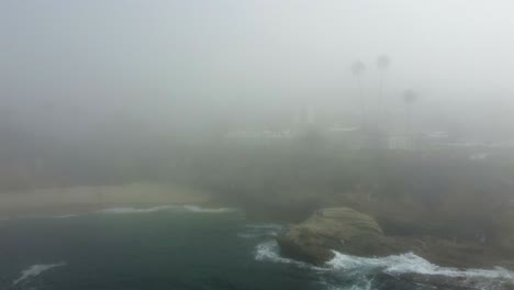 Aerial-View-of-Thick-Morning-Fog-Above-Pacific-Ocean-and-Cliffs-of-Laguna-Beach-and-Waterfront-Resort,-California-USA