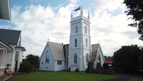 Approach-to-white-old-wooden-historic-church-building-with-New-Zealand-flag-in-Auckland-city