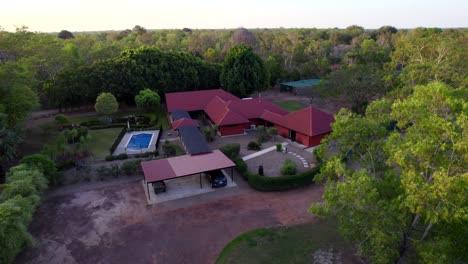 Drone-shots-of-a-rural-estate-with-a-red-house,-pond,-swimming-pool,-stone-gardens-and-green-lawns