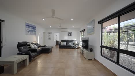 Large-living-room-with-tiled-floors,-white-walls-and-black-leather-couches