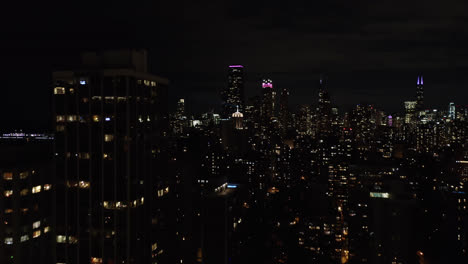 A-drone-captured-the-multiple-lit-buildings-or-skyline-in-the-month-of-October-in-Chicago,-Illinois,-at-dark,-at-night-time